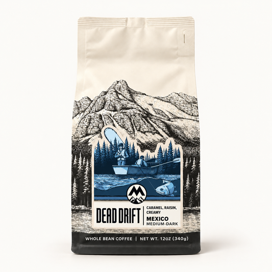 A 12 oz bag of Dead Drift Coffee on a clean white background. The packaging features an illustration of a mountain range and a lake scene with a fishing boat, with the brand logo 'Dead Drift' and flavor details 'Caramel, Basil, Creamy' and 'Mexico Medium Dark' printed on the front.