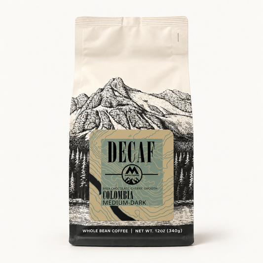 A 12 oz bag of Decaf Colombia Medium-Dark whole bean coffee, featuring a cream-colored background with a black line-art mountain illustration and a central beige label.